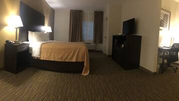 Habitación de hotel con cama, lámparas de noche, escritorio con silla, televisor y ventana con cortinas.