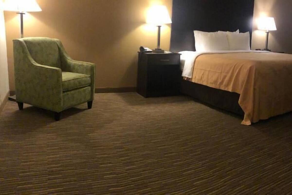 A hotel room with a bed, a chair, a nightstand, and two lamps.