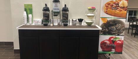 A self-serve beverage station with hot and cold options, a fresh sign, and a healthy apple advertisement.