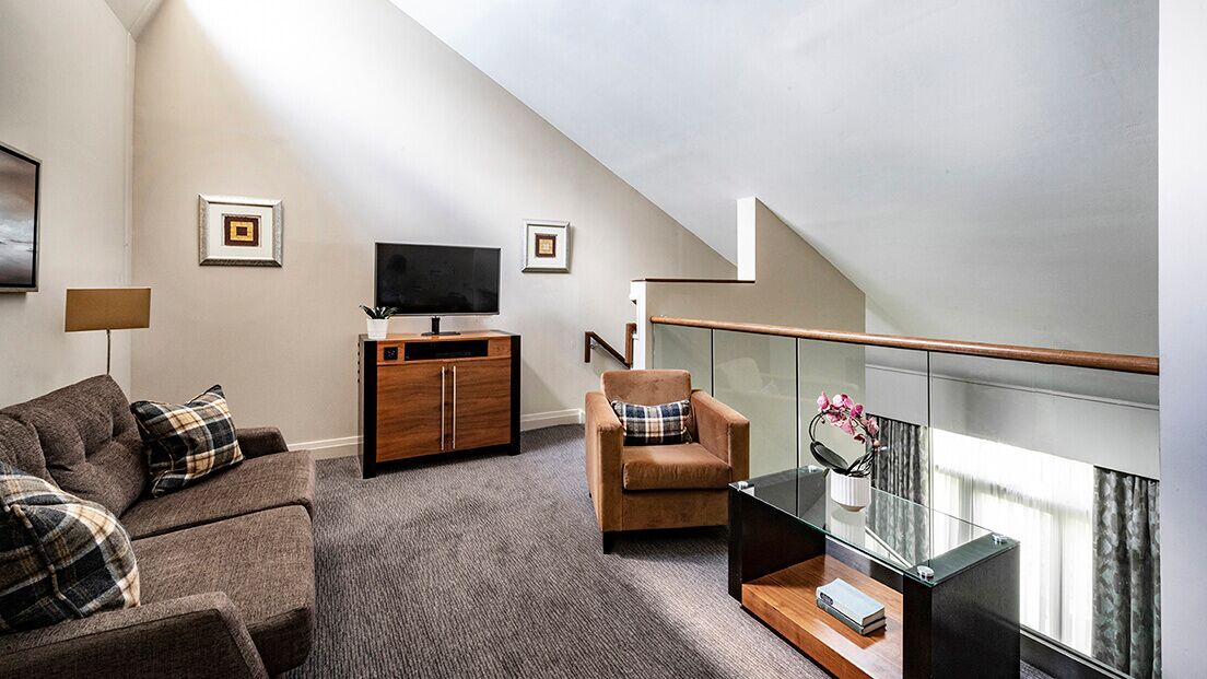 A modern living room with a sofa, armchair, TV, and a glass table with a vase.