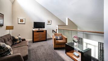 A modern living room with a sofa, armchair, TV, and a glass table with a vase.