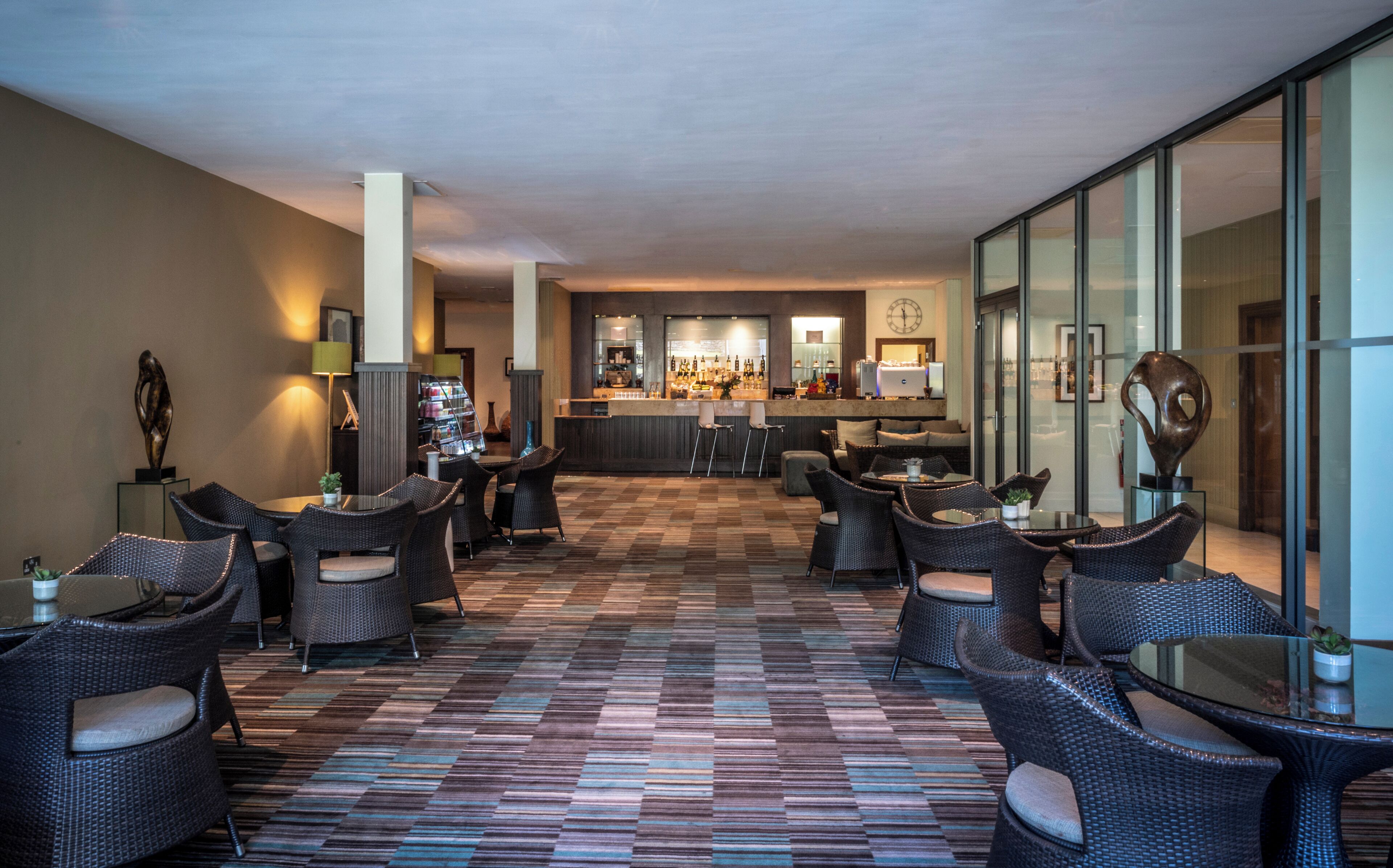 Un vestíbulo de hotel con una zona de bar, espacios de descanso y una alfombra estampada.