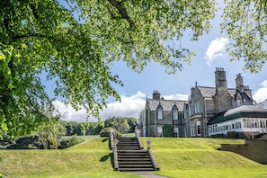 A large, historic building with a prominent staircase leading to the entrance, surrounded by lush greenery and a clear sky. - Norton House Hotel & Spa (Newbridge)