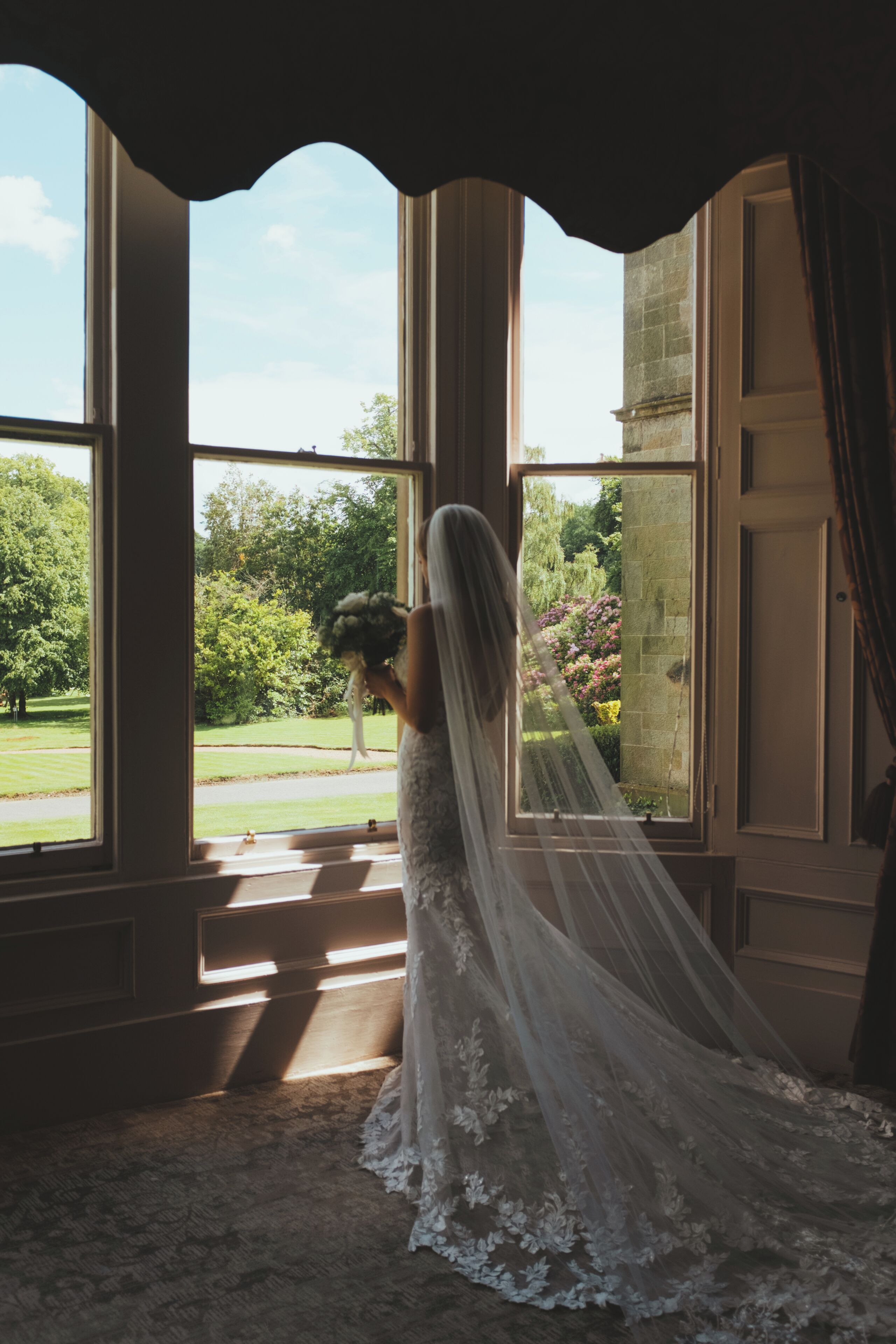 Una habitación con ventanas amplias, vista a zonas verdes y una persona con un vestido de novia.