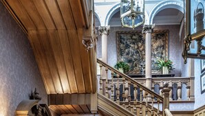 A grand staircase with ornate railings, a fireplace with a mantel, and a patterned carpet.