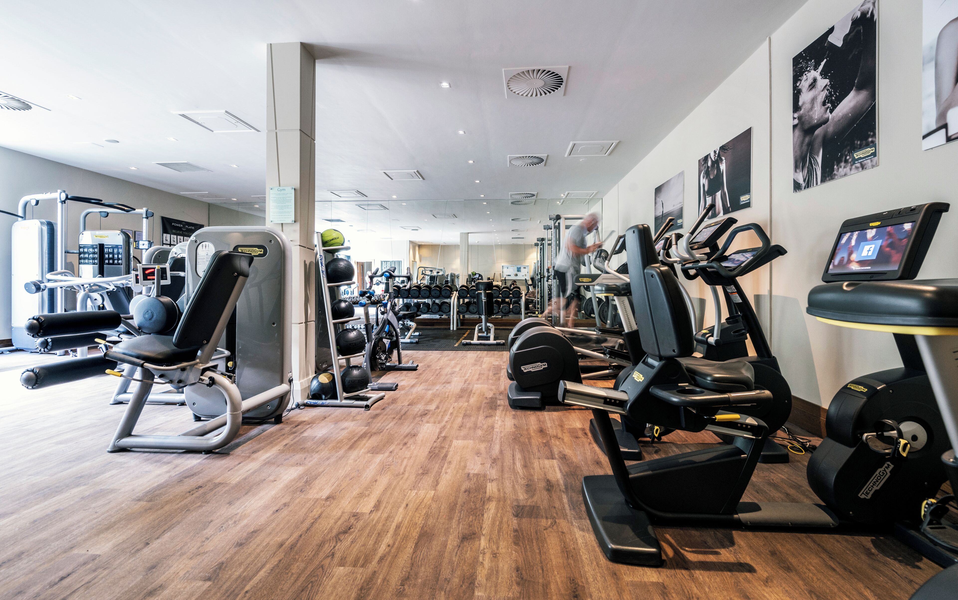 Ein Fitnessstudio mit Herz-Kreislauf-Geräten, Krafttrainingsgeräten und Holzboden.