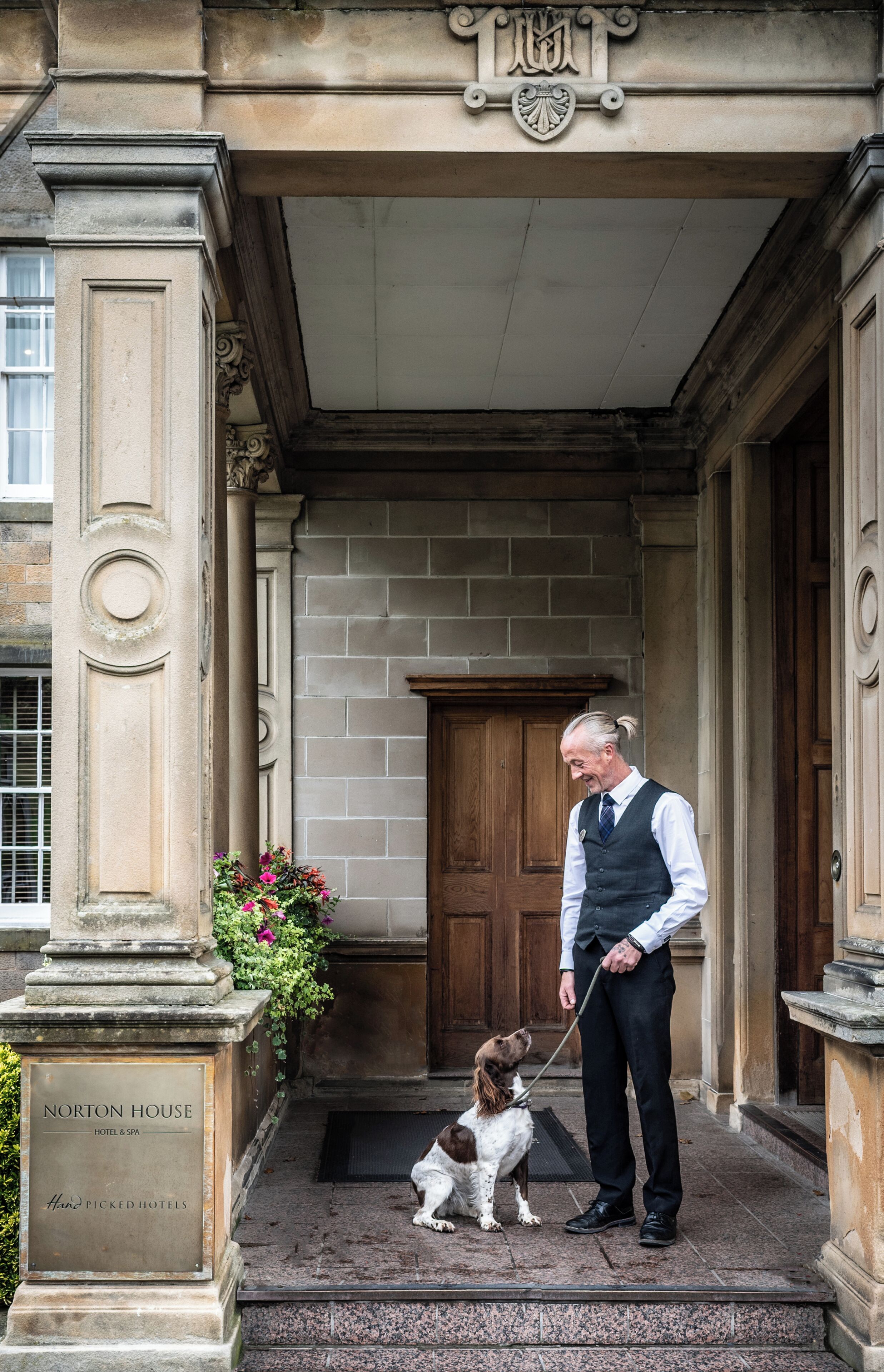 Ein Mann mit Hund vor einem Gebäude mit der Aufschrift 'Norton House Hotel & Spa'.