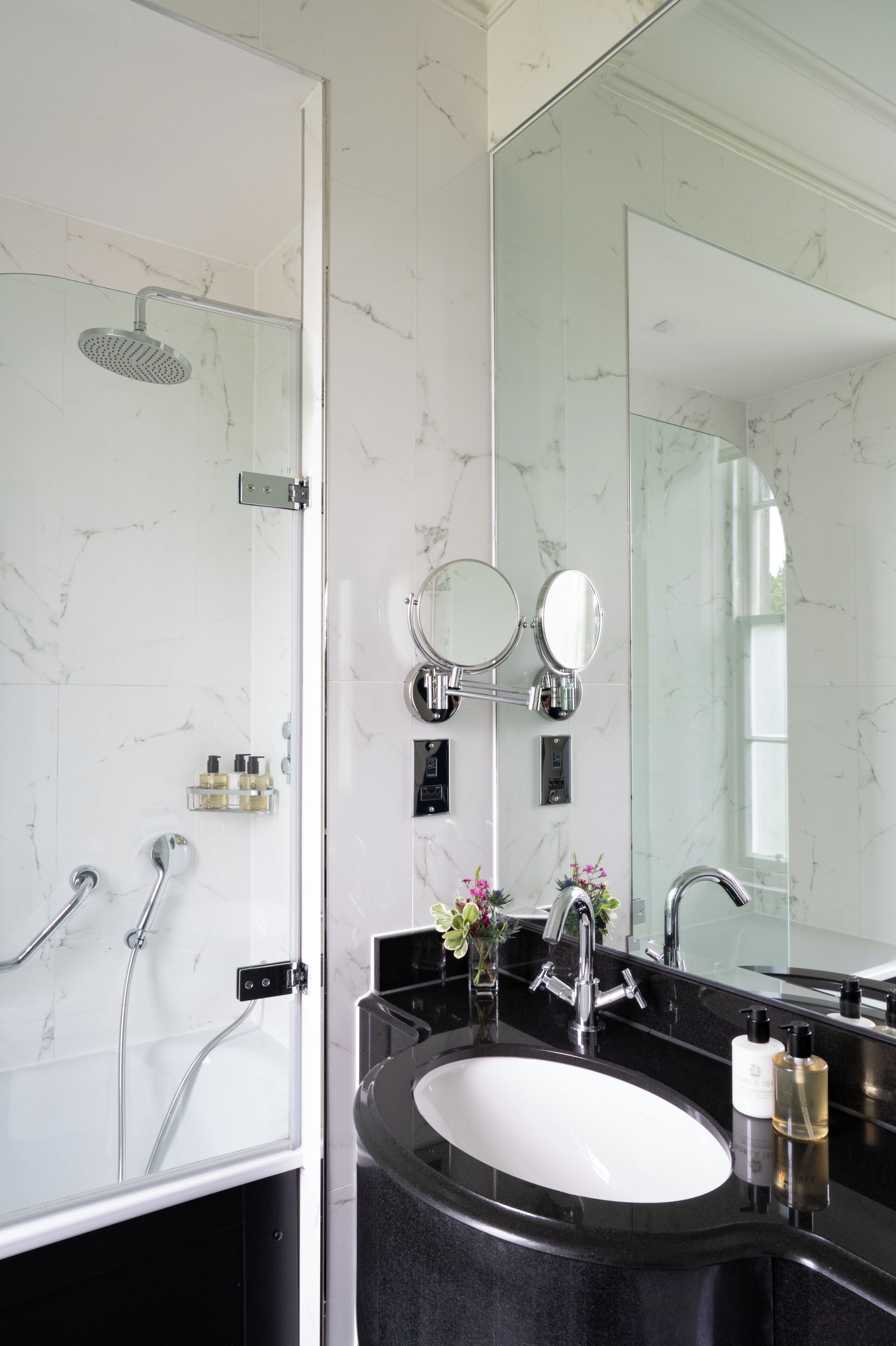 A bathroom with a glass-enclosed shower, a black sink, and a large mirror.