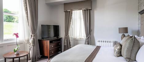 Ett hotellrum med en säng, en tv, ett litet bord med en vas och gardiner.