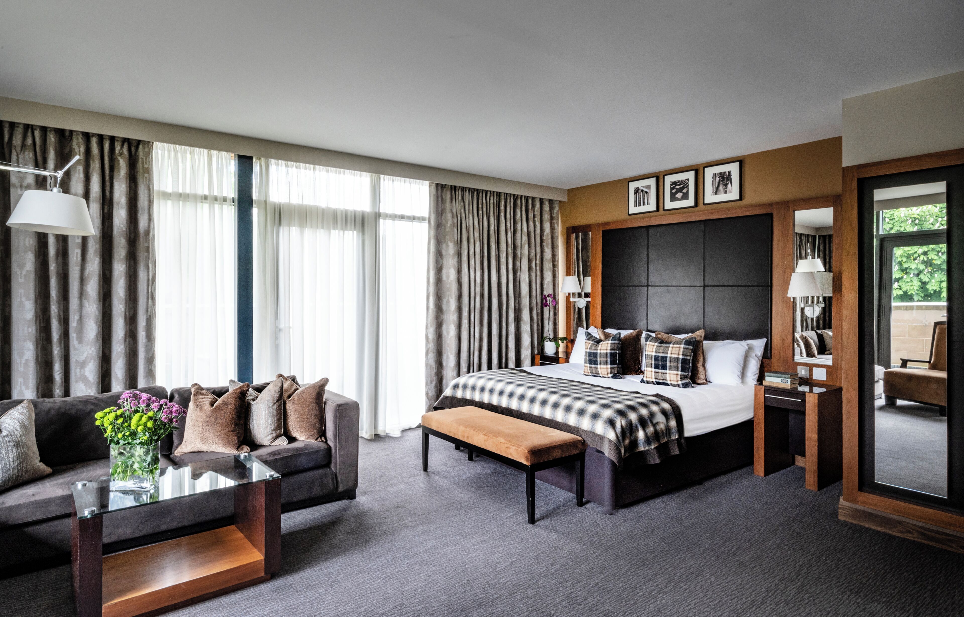 A hotel room with a bed, a sofa, a coffee table, and a large window with curtains.