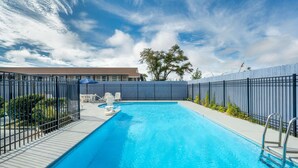 Une piscine rectangulaire avec une échelle métallique sur un des côtés, entourée d’une clôture et avec un bâtiment visible en arrière-plan.