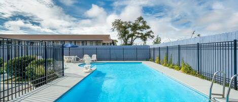 Una piscina rectangular con una escalera metálica en un lateral, rodeada por una valla y un edificio al fondo.