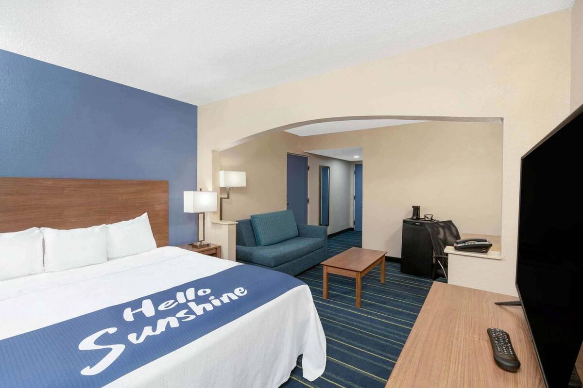 A hotel room with a bed, a desk, a TV, a remote, and a couch.