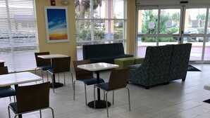 Un espace de détente intérieur moderne, avec des tables et des chaises, un canapé et une grande fenêtre équipée de stores.
