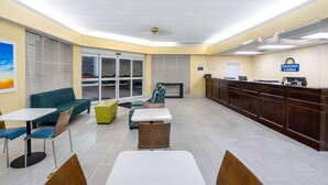Un hall d’hôtel comprenant un comptoir d’accueil, un espace salon avec des tables et des chaises, et une grande fenêtre équipée de stores.