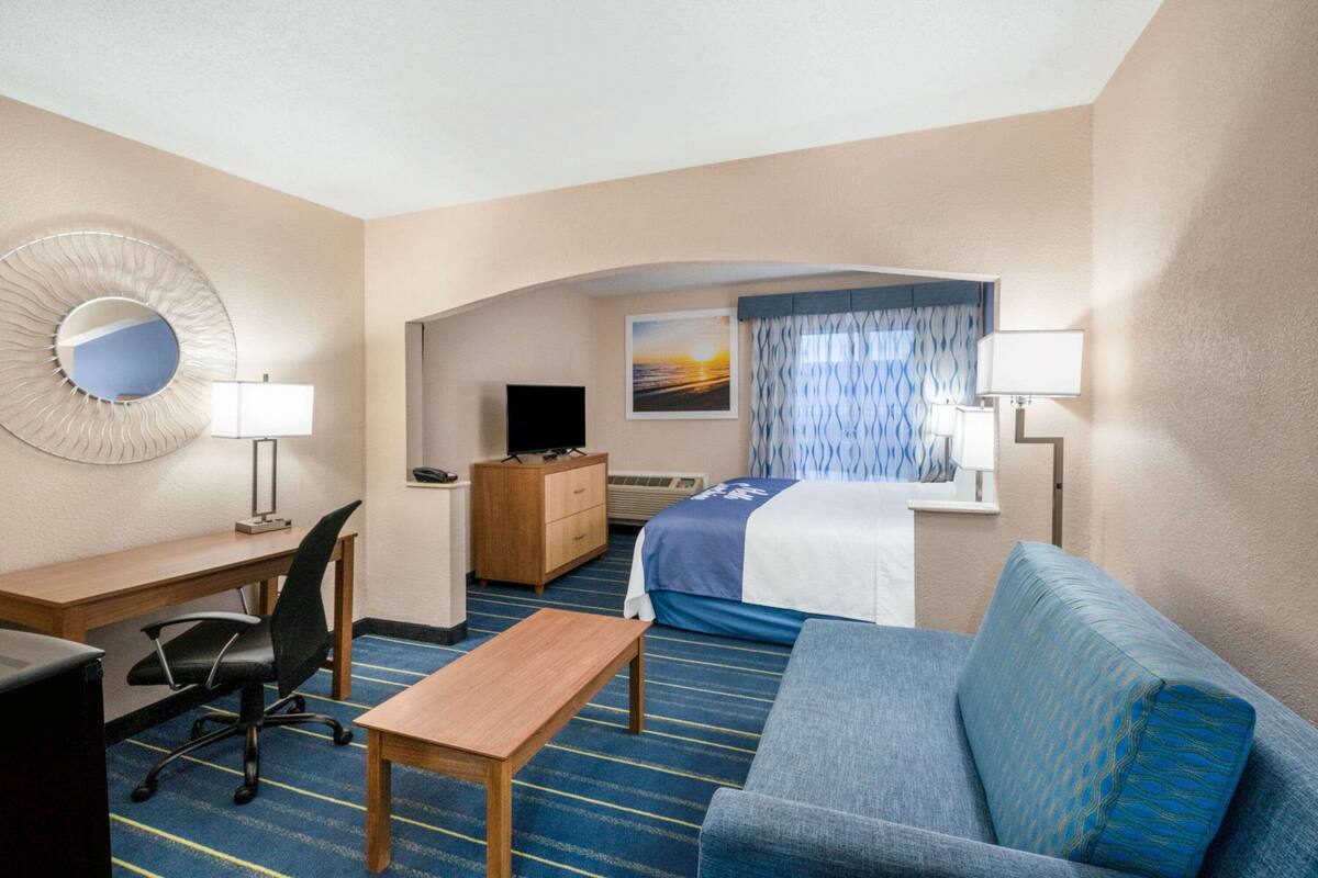 A hotel room with a desk, chair, bed, and a sofa.