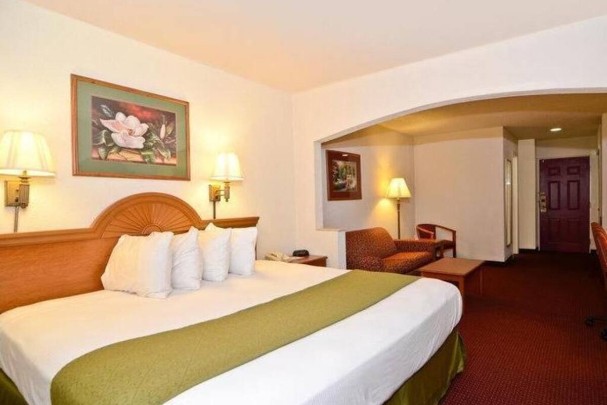 A hotel room with a large bed, two bedside lamps, a chair, and a door leading to another room.