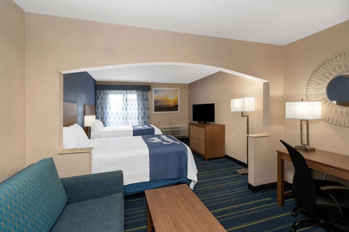 A hotel room with two beds, a desk, a chair, a TV, and a desk lamp.