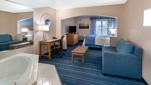 Une chambre d’hôtel dotée d’un grand lit, d’un coin salon avec un canapé et un fauteuil, d’un bureau avec une chaise, d’une télévision et d’une salle de bain avec une baignoire.