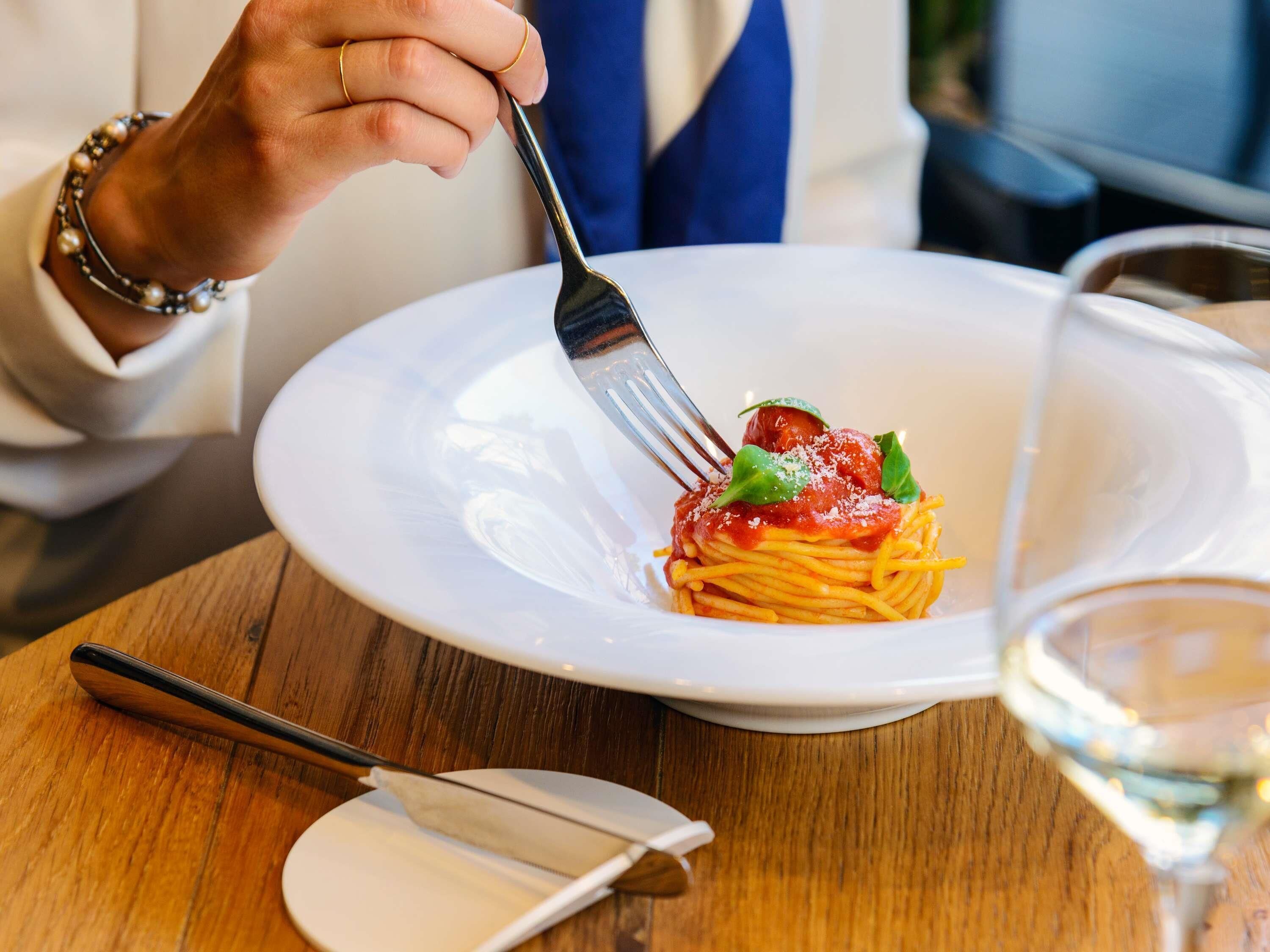 A person dining at a table with a plate of spaghetti and a fork.