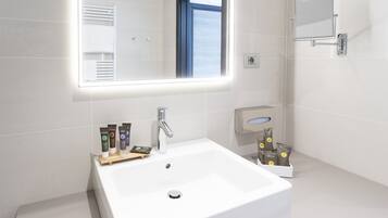 Une salle de bain moderne avec un lavabo blanc, un miroir et des articles de toilette posés sur le comptoir.