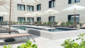 A modern pool area with multiple lounge chairs and umbrellas, surrounded by a building with large windows.
