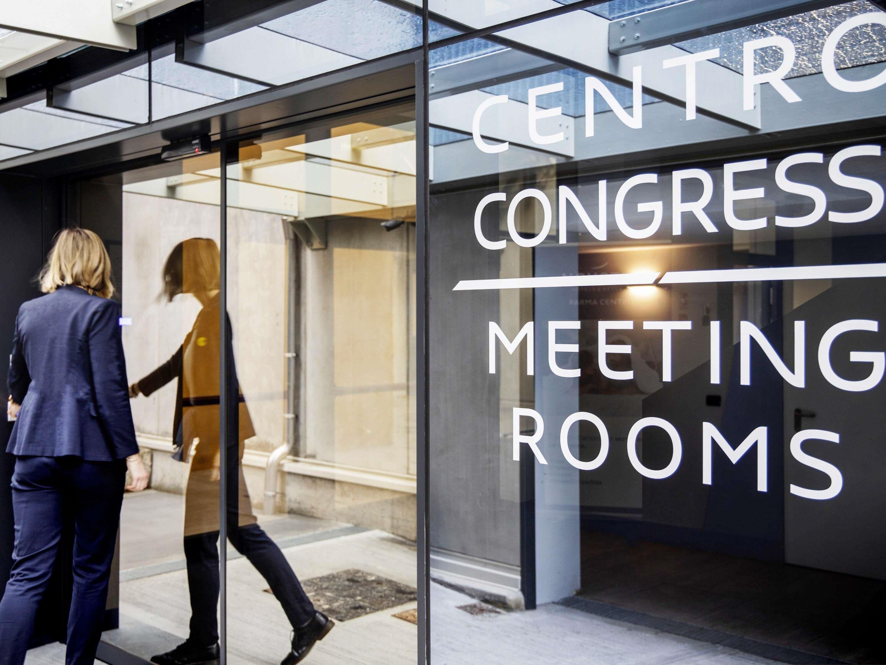 L’entrée d’un bâtiment, avec une enseigne indiquant : « SALLES DE RÉUNION – CENTRO CONGRESS ».