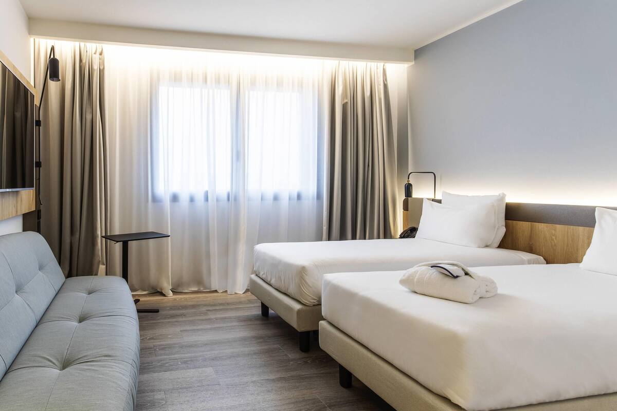 A hotel room with two beds, a sofa, a small table, and a lamp.