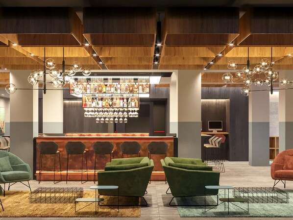 Eine Bar mit einer Auswahl an Flaschen und Gläsern, grünen gepolsterten Stühlen und einem modernen Deckenstil.