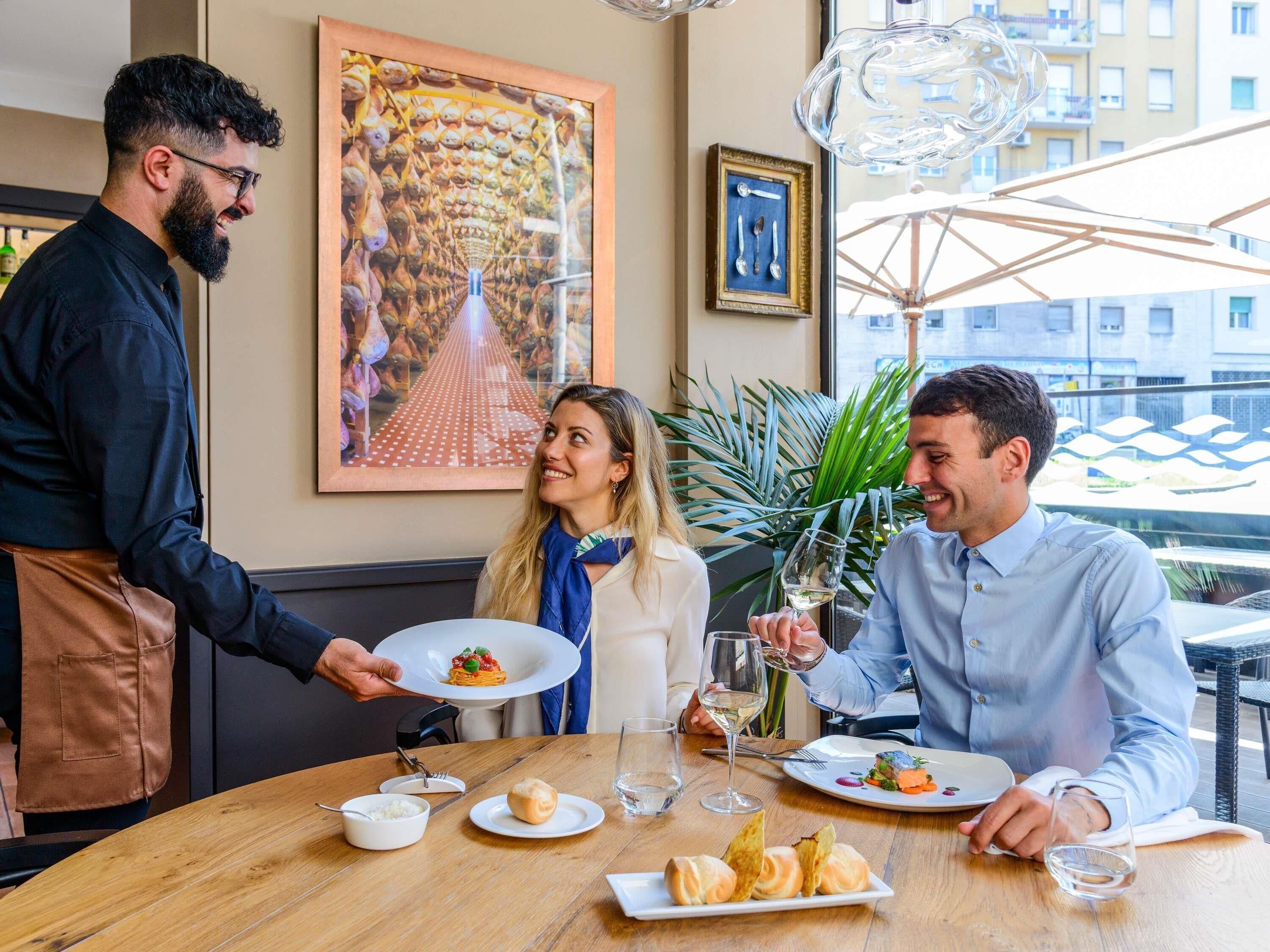 Une scène dans un restaurant, où un serveur apporte des plats aux clients assis à une table.