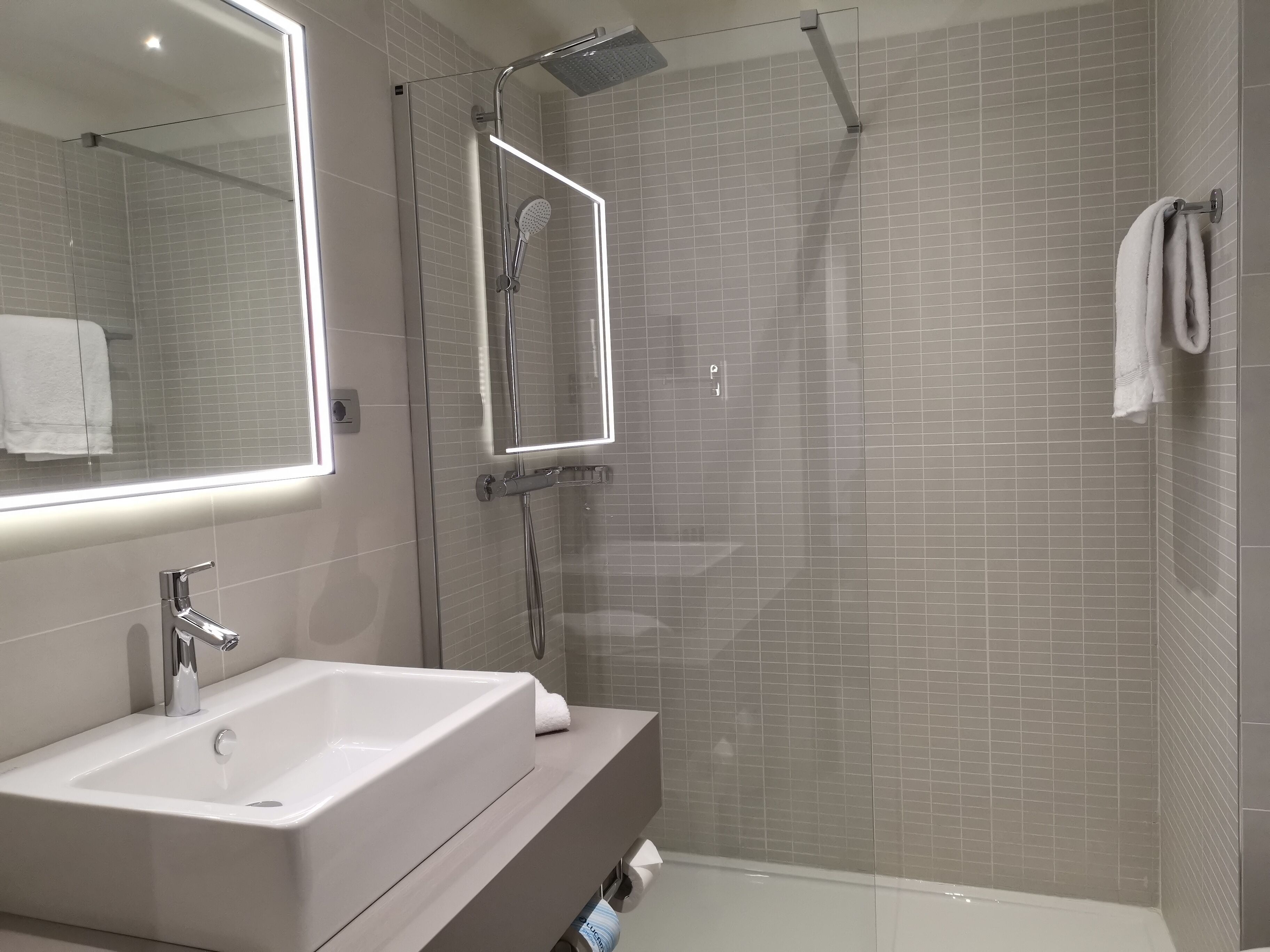 A modern bathroom with a large mirror, a white sink, a shower with a glass door, and a towel rack.