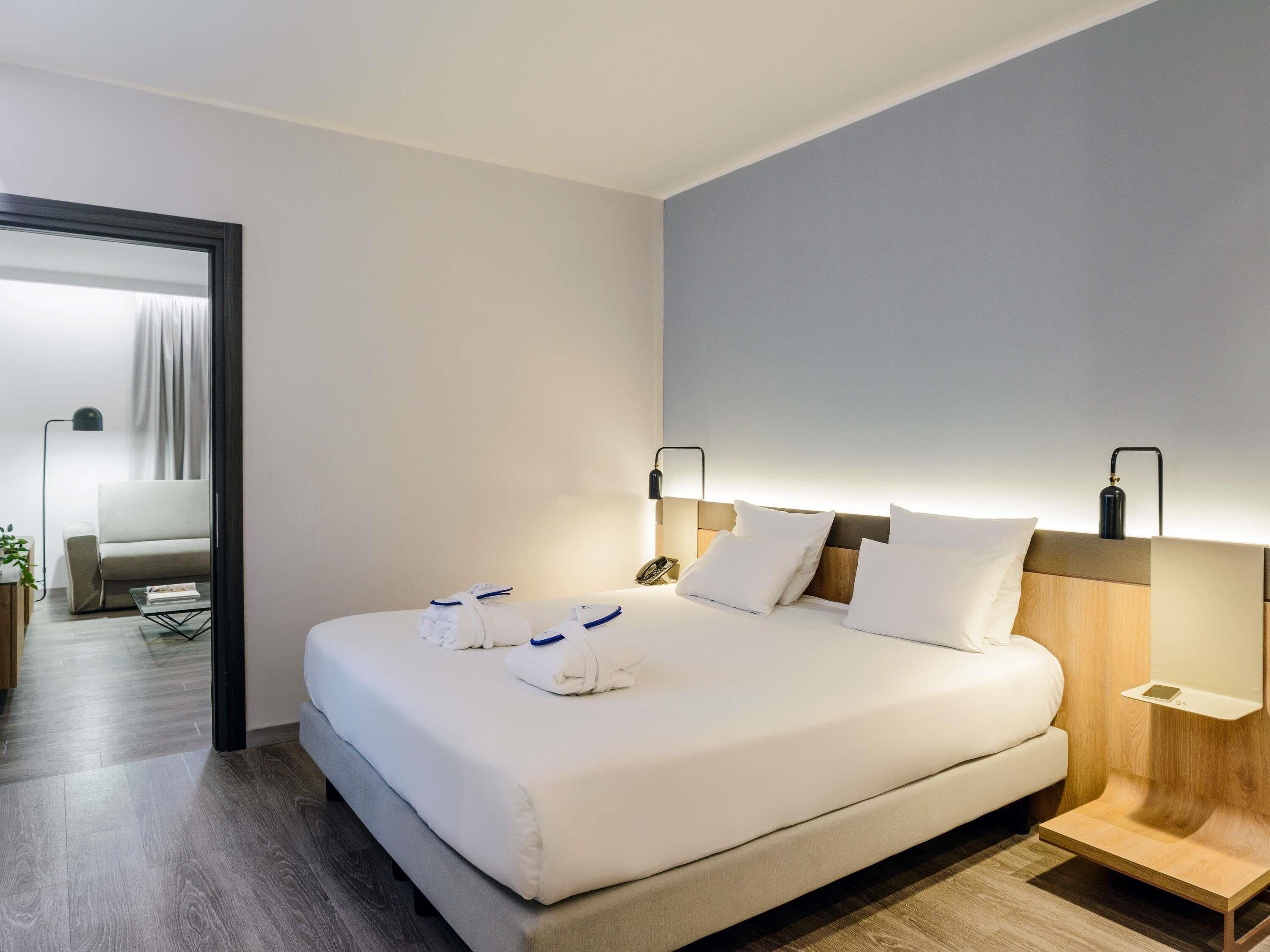 Une chambre d’hôtel moderne, dotée d’un grand lit, de tables de chevet, d’un bureau et donnant sur le couloir.