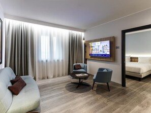 A modern hotel room with a sofa, armchair, coffee table, and a TV mounted on the wall. - Novotel Parma Centro (Parma)