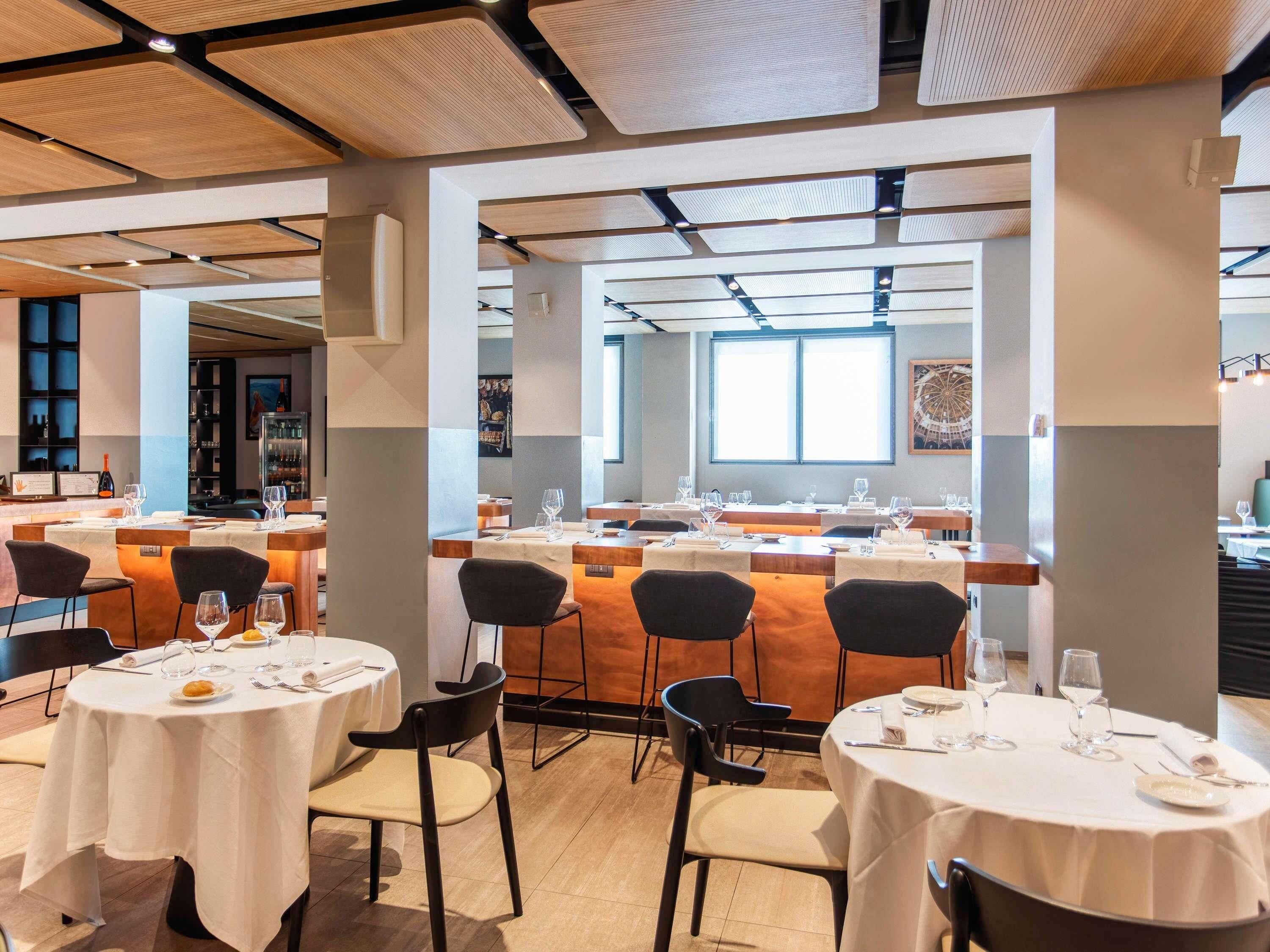 A restaurant with round tables, black chairs, and a bar area.