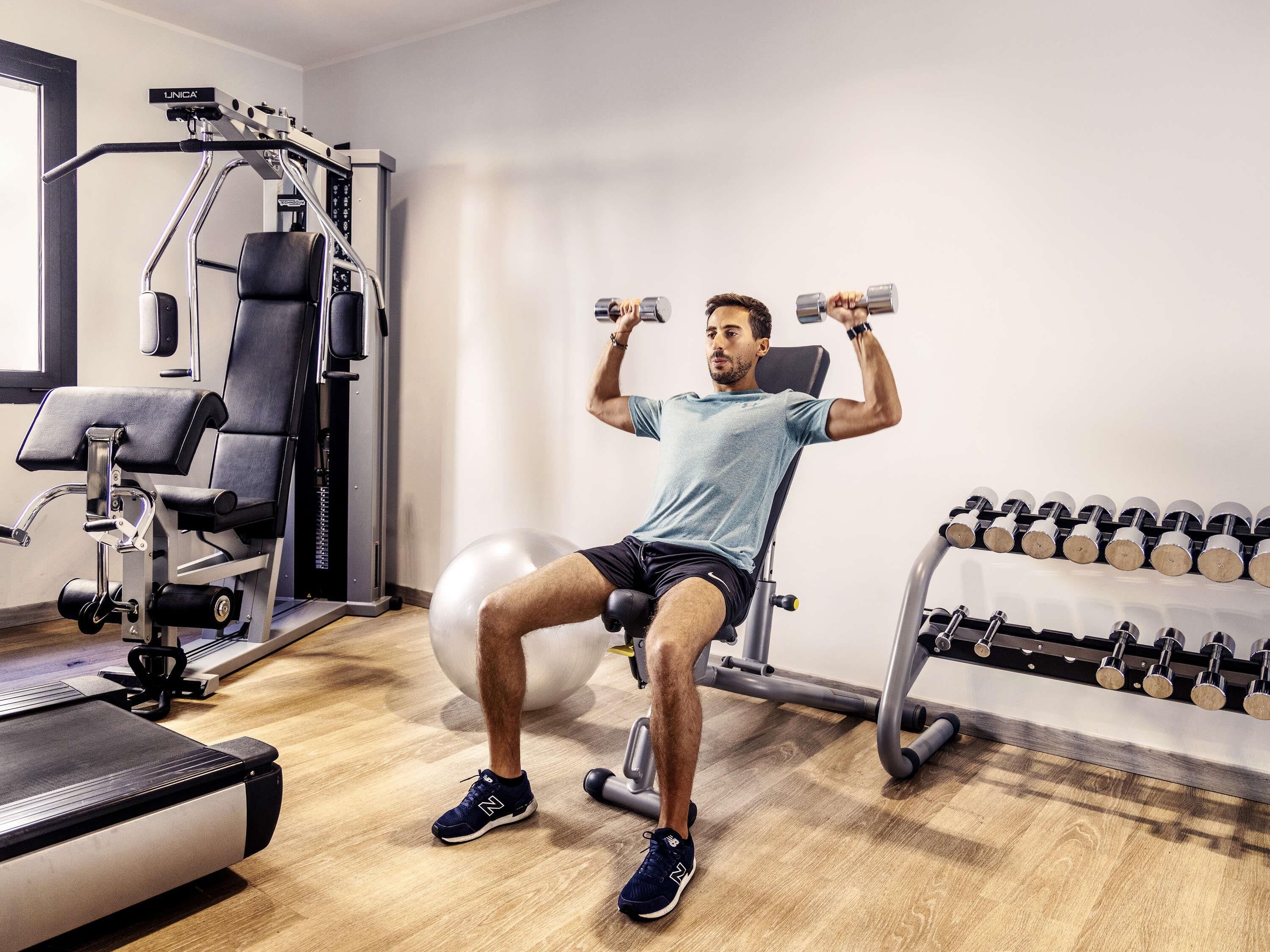 Ein Fitnessraum mit Trainingsgeräten, einer Bank und Kurzhanteln.