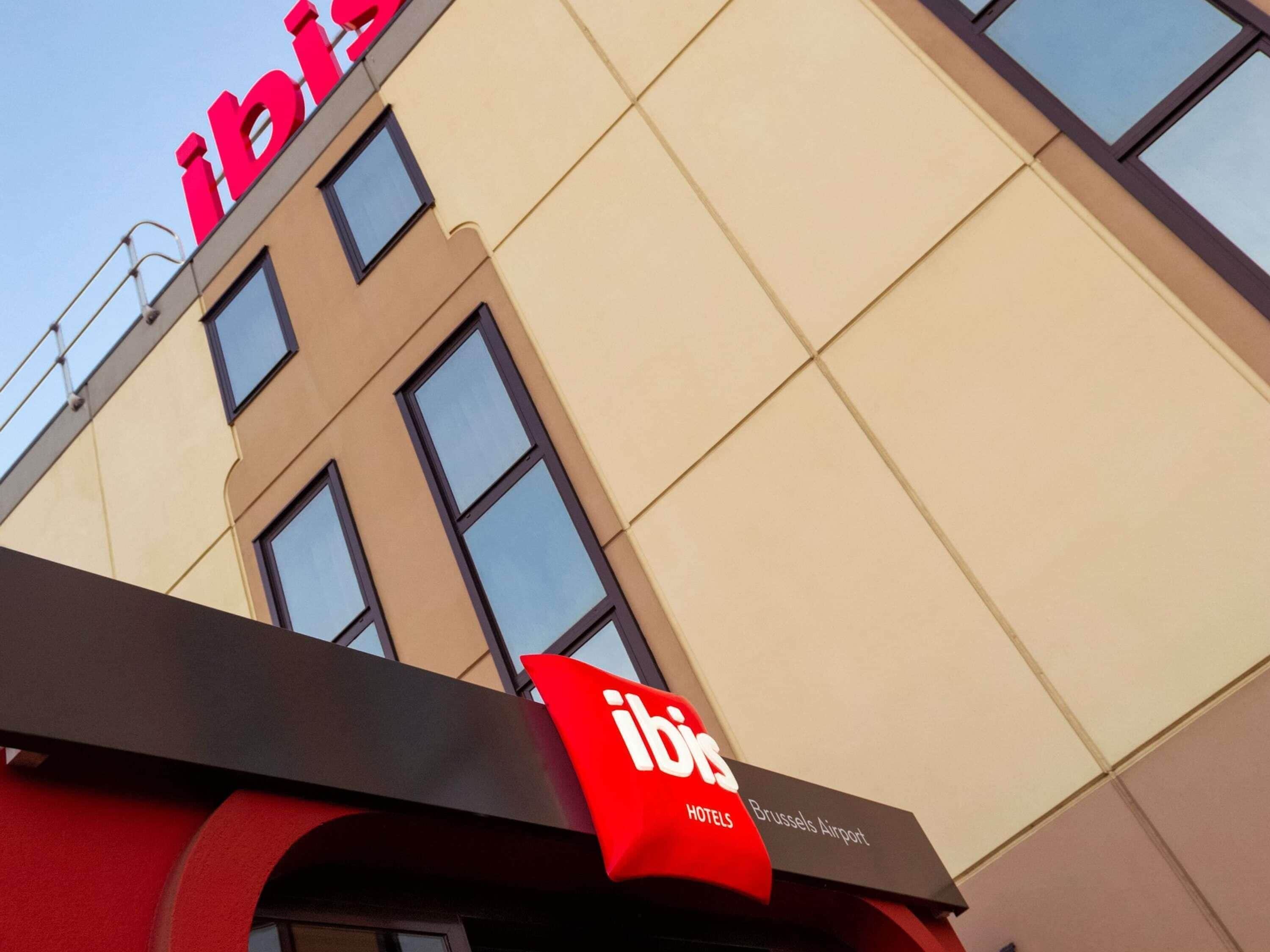 A hotel with a prominent red logo, multiple windows, and a sign indicating it's located at Brussels Airport.
