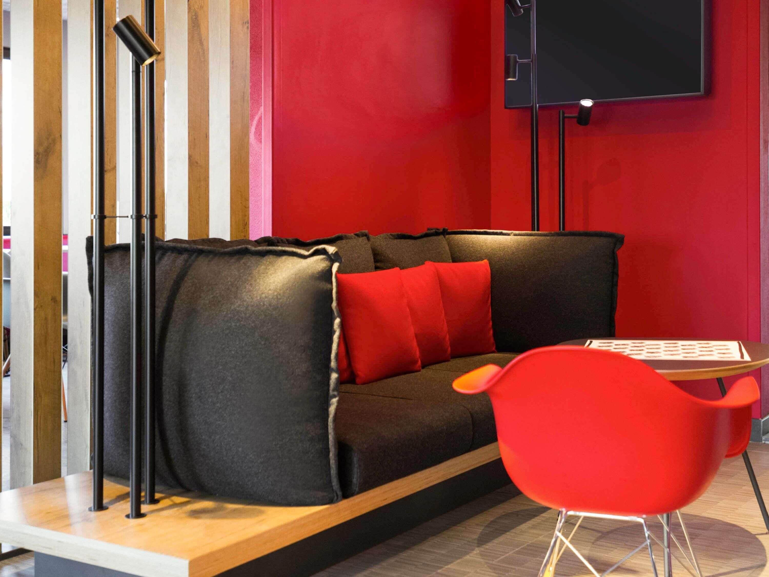 A modern room with a black sofa, red cushions, a red chair, a wooden table, and a black floor lamp.