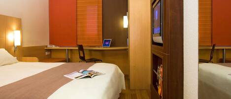 A hotel room with two beds, a desk with a laptop, a TV, and a magazine on the bed.