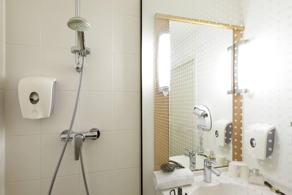 Un bagno con doccia, portasciugamani, asciugacapelli e lavandino con specchio.
