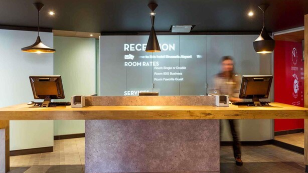 A reception desk with a digital screen displaying room rates and services. - ibis Brussels Airport (Machelen)