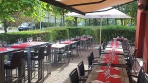 An outdoor dining area with tables set for two, covered by a canopy, and surrounded by chairs. - ibis Brussels Airport (Machelen)