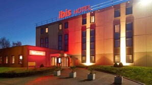 A modern hotel building with a prominent 'Ibis Hotel' sign, a well-lit entrance, and a landscaped area with potted plants. - ibis Brussels Airport (Machelen)