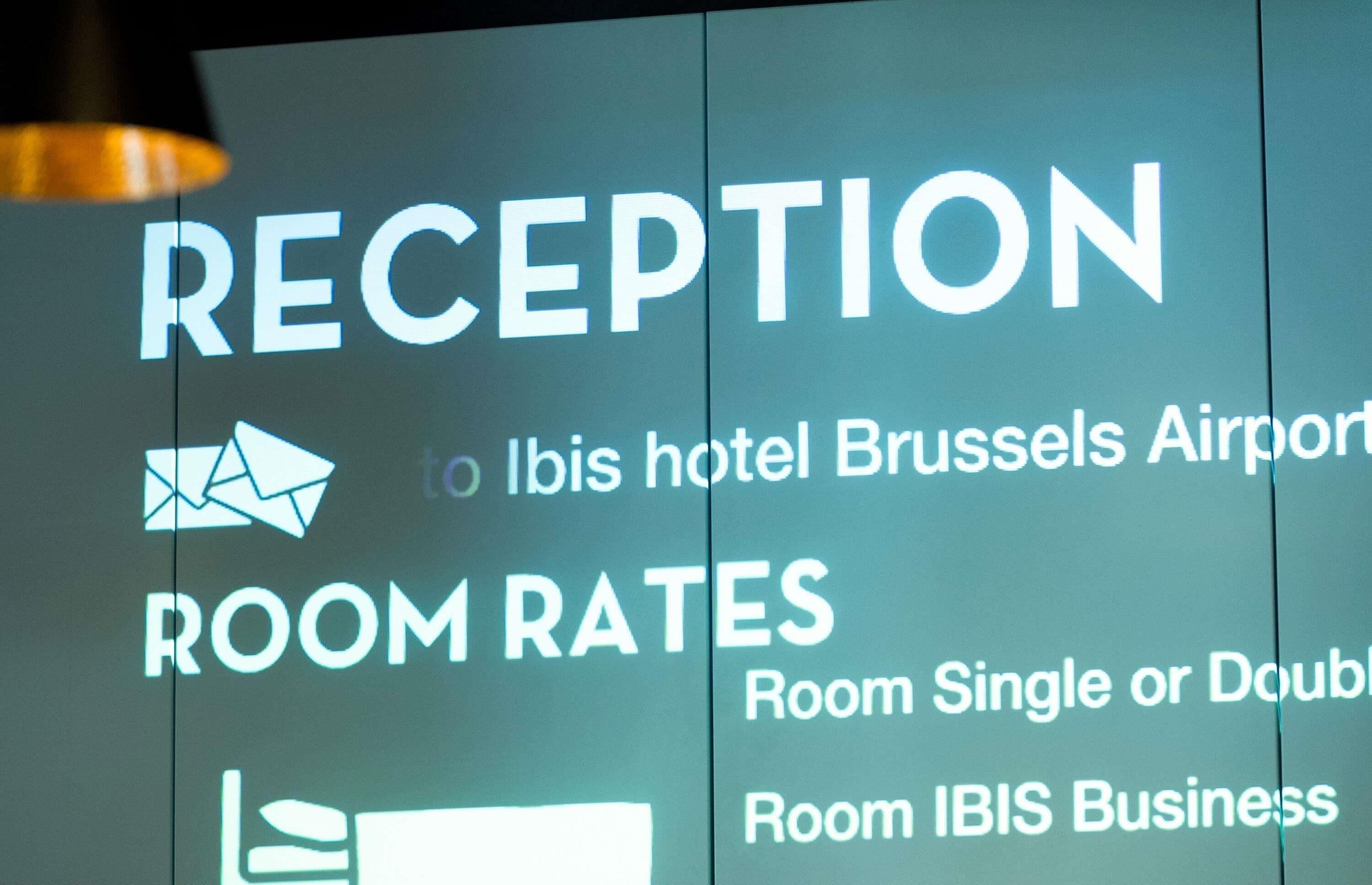 A sign with the word "RECEPTION" and mentions "IBIS hotel Brussels Airport" and "ROOM RATES" for single or double rooms and IBIS Business.
