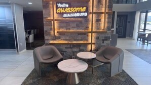 A lobby with a neon sign, two round tables, and modern chairs.