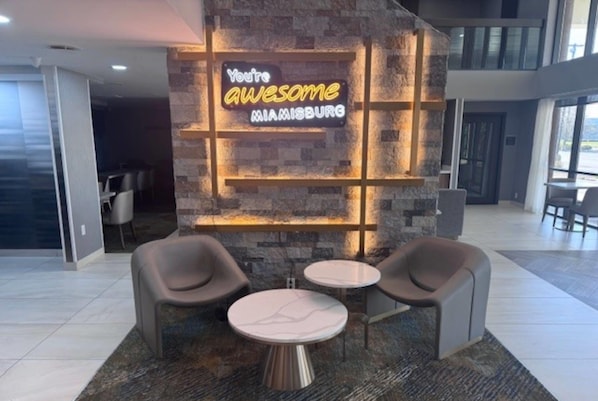 A lobby with a neon sign, two round tables, and modern chairs.