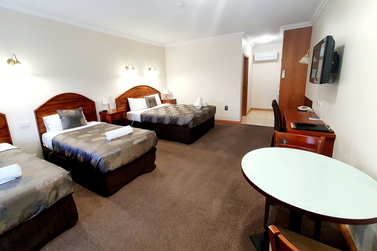 A hotel room with two beds, a desk, a chair, a TV, and a carpeted floor.