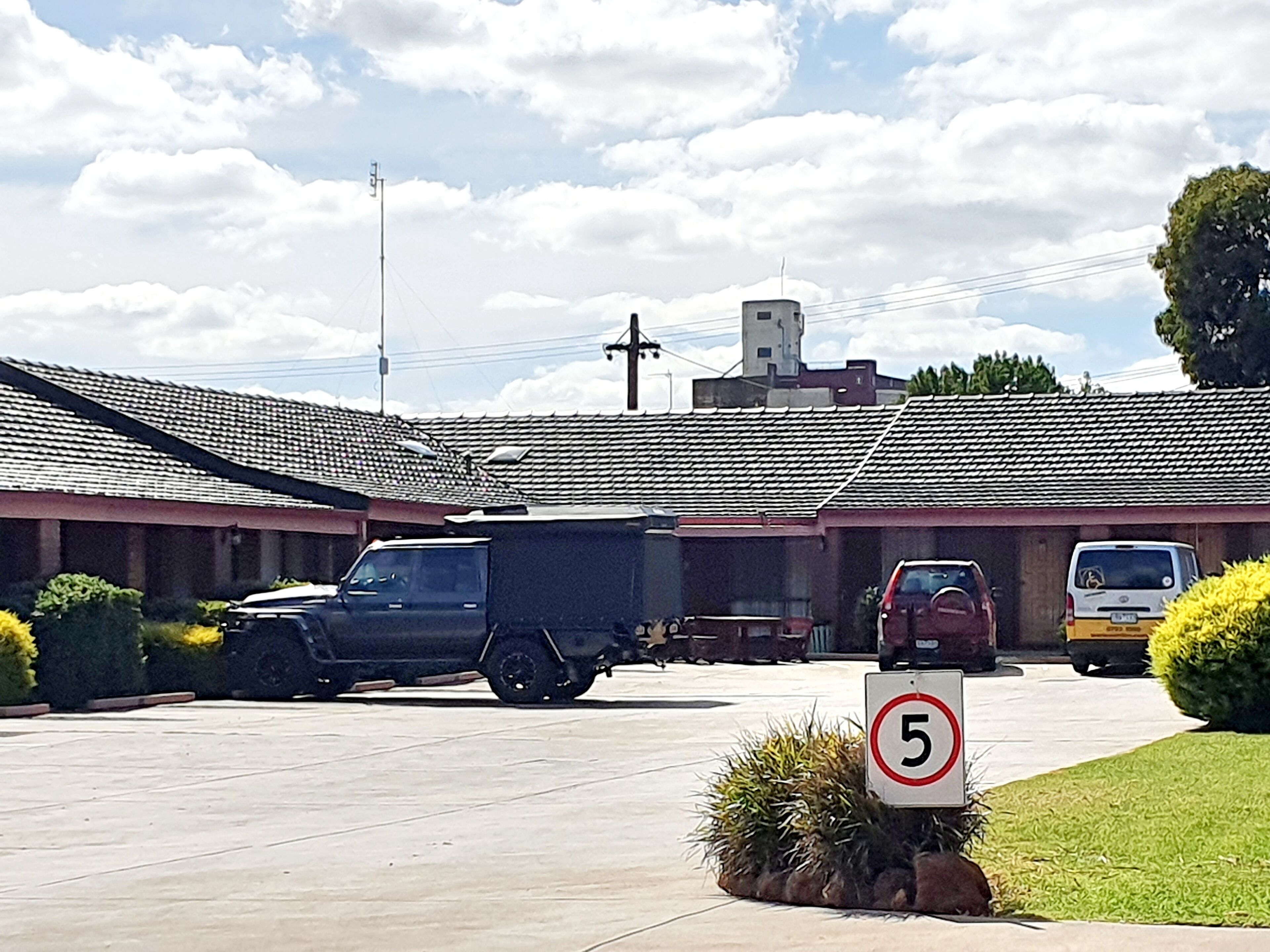 Un estacionamiento con un letrero de límite de velocidad, una camioneta y una furgoneta frente a un edificio con tejado de tejas.