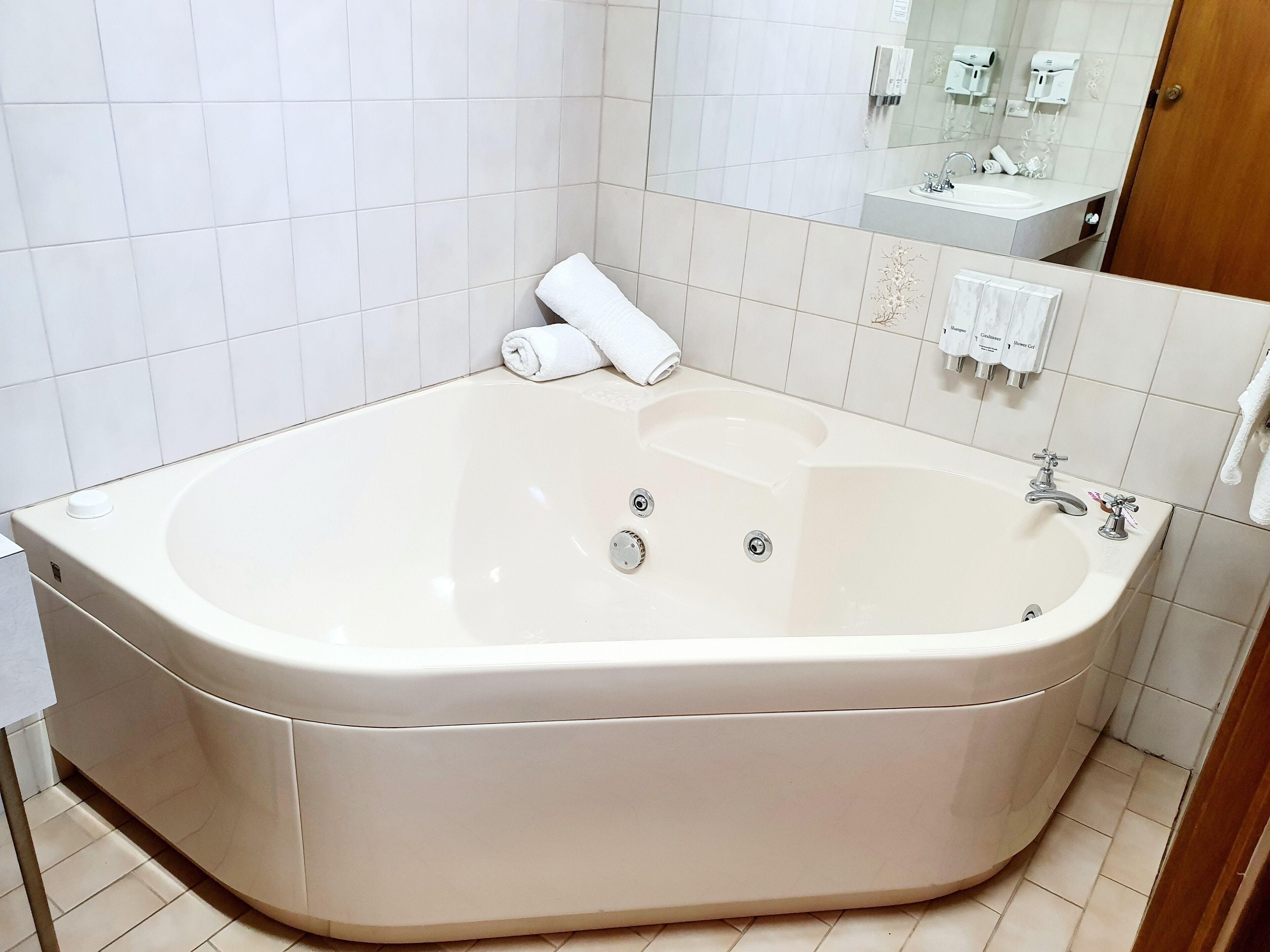 A large, white bathtub with two faucets and a control knob, a towel, and a mirror above the sink.
