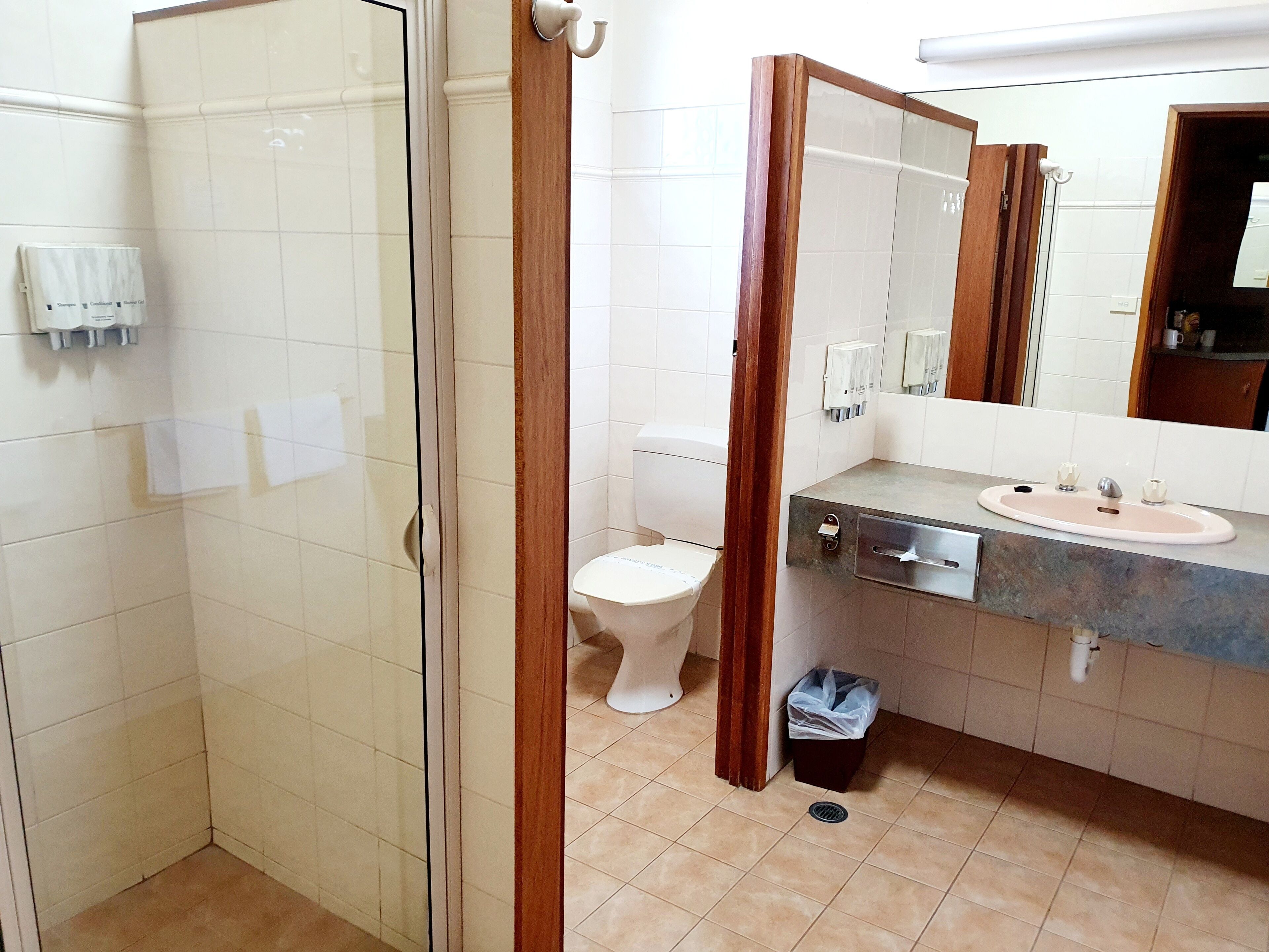 A bathroom with a glass shower enclosure, a toilet, a sink with a mirror, and a trash bin.