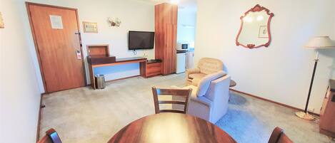 A compact living space with a dining table, two chairs, a sofa, a TV, and a small kitchenette.